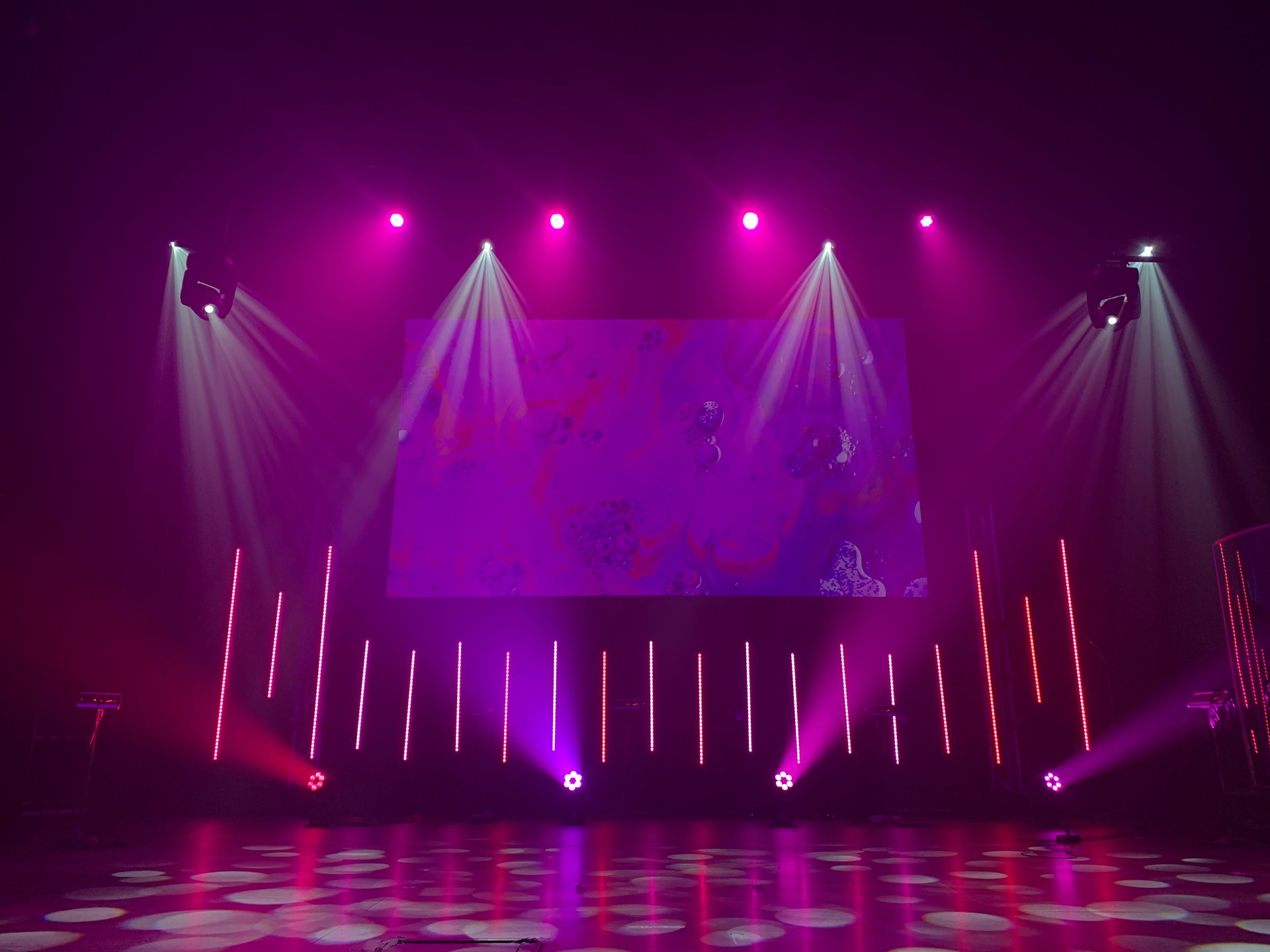 Licht en Geluid Verhuur 5 Tips voor een Onvergetelijk Feest! Een podium met paarse verlichting en een groot scherm. Een betoverende setting voor een spectaculaire show. Een voorbeeld van een licht en geluid set in de verhuur.